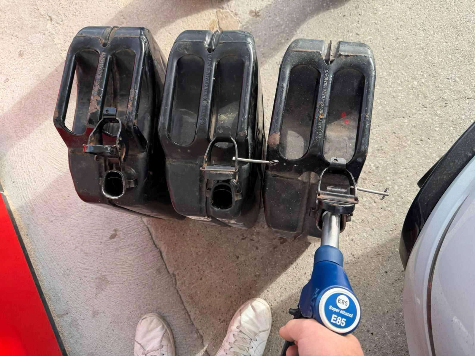 3 petrol cans, one is being filled up from a pump labelled superethanol E85